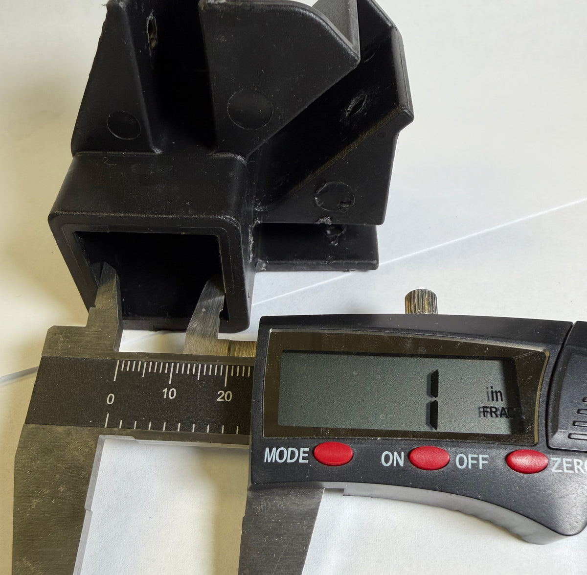 A black plastic square block part shown next to a digital caliper and a digital micrometer, indicating its dimensions are approximately 1 millimeter.