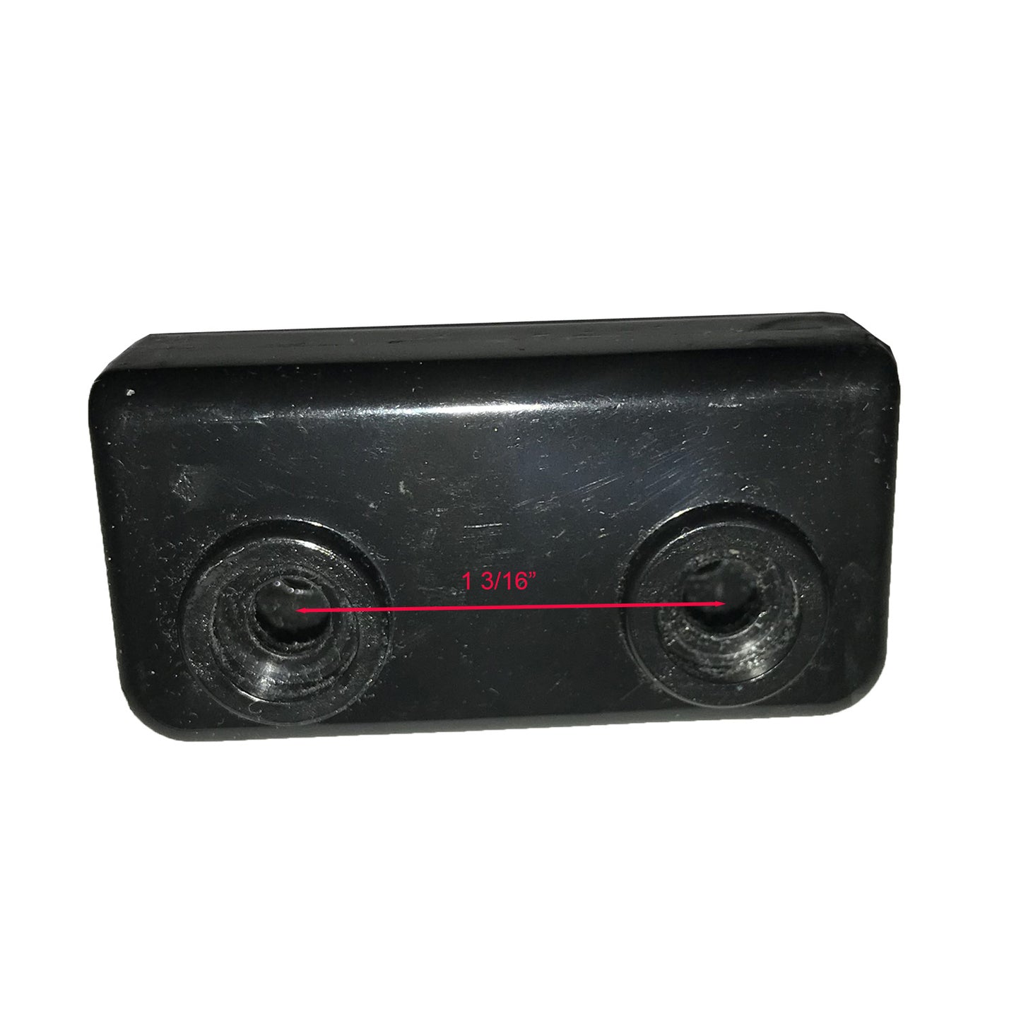 The image shows a black rectangular object with a textured surface and rounded corners. There are two circular indents, possibly screw holes, one on each end. A red line with a measurement marking "1 3/16'" spans the length between the centers of these indents, indicating their separation distance.